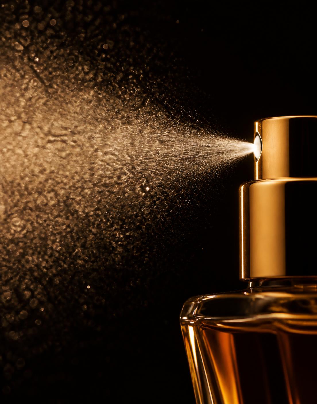 Perfume mist suspended in warm light beside an amber bottle